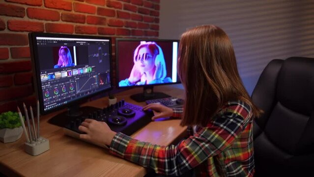 Portrait of young girl at the computer looking in monitors editing video using special equipment mixer.