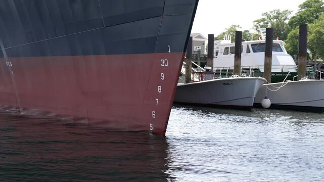 Numbers line up along bow of large ship docked in front of smaller marine vessels