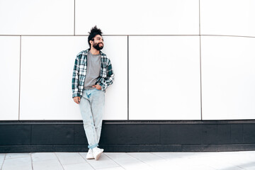 Handsome smiling hipster model. Unshaven Arabian man dressed in summer casual clothes, jeans and shirt. Fashion male with long curly hairstyle posing in the street. Near urban wall