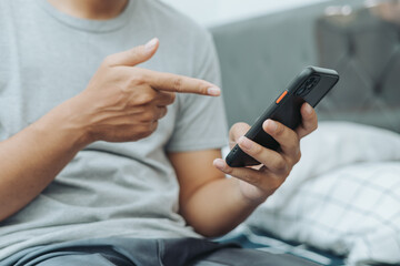Hands of Asian man holding checking touching scrolling smartphone from bed room