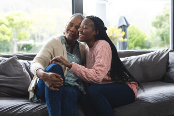 Happy african american senior mother and adult daughter sitting on couch,laughing and embracing