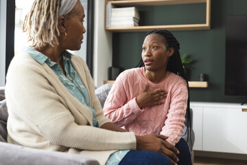 Happy african american senior mother and adult daughter sitting on couch,laughing and talking