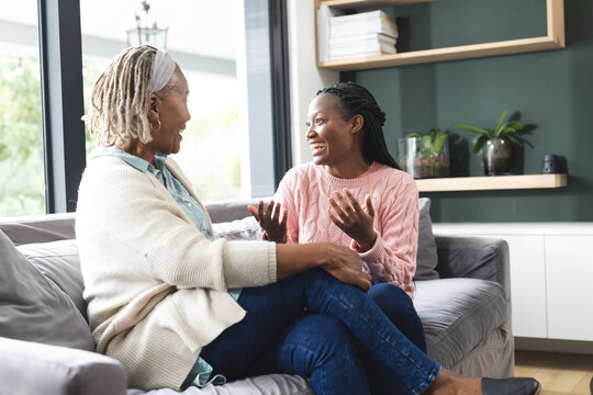 Happy african american senior mother and adult daughter sitting on couch,laughing and talking