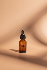 Dark glass cosmetic bottle with a dropper on a white cube podium on beige background. Natural cosmetics concept, natural essential oil and skin care products