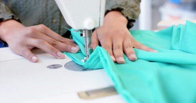 Biracial female fashion designer sewing fabric with sewing machine in studio, slow motion
