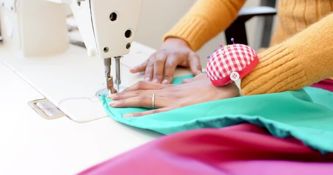 Biracial female fashion designer sewing fabric with sewing machine in studio, slow motion