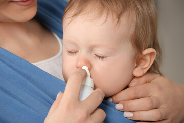 Mother helping her baby to use nasal spray, closeup