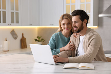 Happy couple with laptop at white table in kitchen