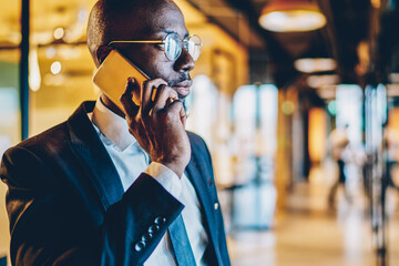 Experienced dark skinned proud ceo in black suit talking on telephone device