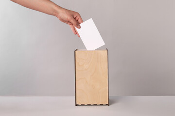 Man putting his vote into ballot box on light grey background, closeup