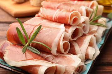 Rolled slices of delicious jamon with rosemary on table, closeup