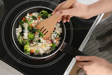 Woman frying rice with vegetables on induction stove, top view