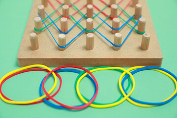 Wooden geoboard with rubber bands on green background, closeup. Educational toy for motor skills...