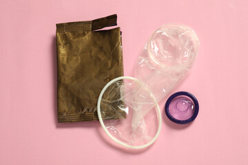 Unpacked female, male condoms and torn package on light pink background, flat lay. Safe sex