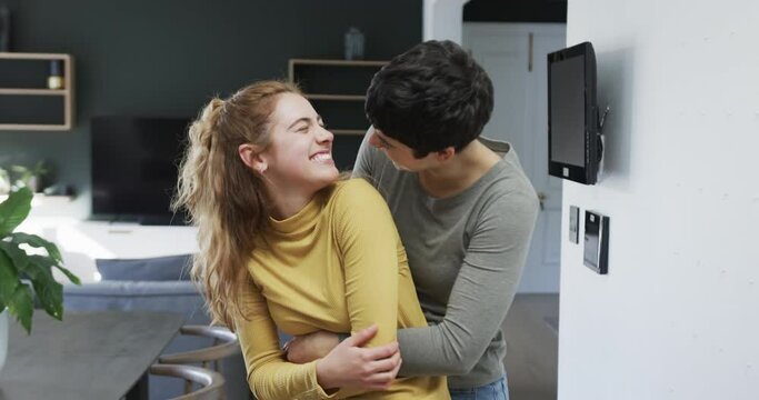 Happy caucasian lesbian couple embracing, smiling and laughing in sunny kitchen
