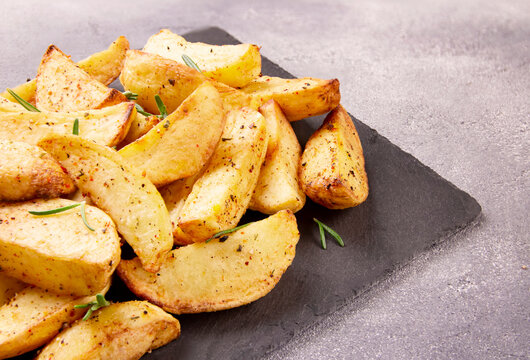 Baked potato wedges with seasonings on a stone tray on a gray stone.