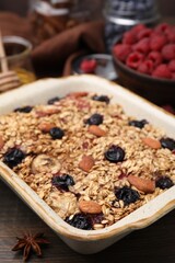 Tasty baked oatmeal with berries and almonds in baking tray on wooden table, closeup