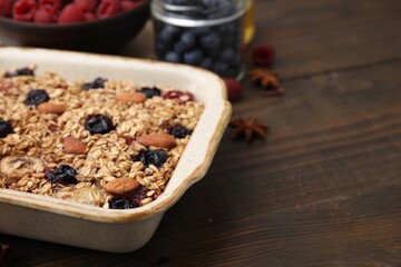 Tasty baked oatmeal with berries and almonds on wooden table in baking tray, closeup. Space for text