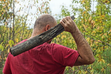 one healthy aggressive bald man in a red t-shirt holds a dirty large heavy wooden club behind his...