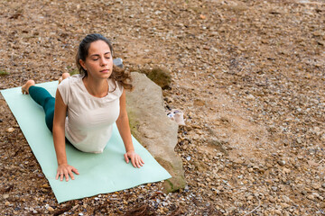A young and beautiful girl practicing yoga exercises by the river in the early morning.