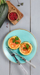 Baked zucchini with cheese and tomatoes on a gray wooden table, served on a ceramic plate with utensils. Fresh and appetizing, perfect for a gourmet meal