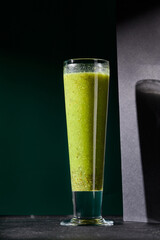 Vibrant green smoothie with apple and kiwi, elegantly presented in a glass on a shadowed black backdrop