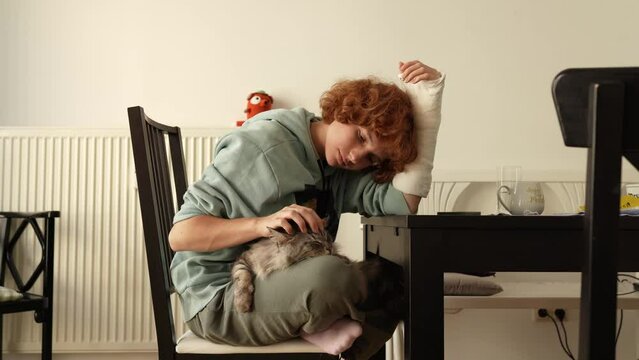 Portrait teenage girl with red hair, cast on arm and domestic cat at home