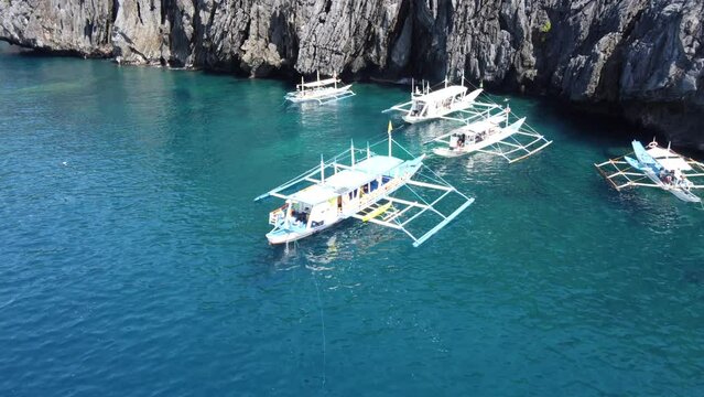 Traditional Outrigger Island hopping Tour Boats anchored at the secret beach, El Nido Philippines. Aerial dolly in