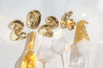 Happy New Year flat lay, text 2024 golden balloons on light grey background, sparkling wine bottle,...