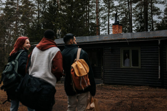 Rear view of friends walking towards haunted cabin during vacation