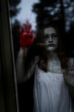 Female ghost with blood on hand seen through window of haunted cabin