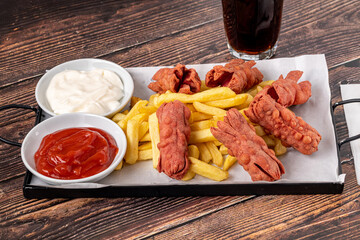 French fries and deep fried sausage with ketchup and mayonnaise on wooden table