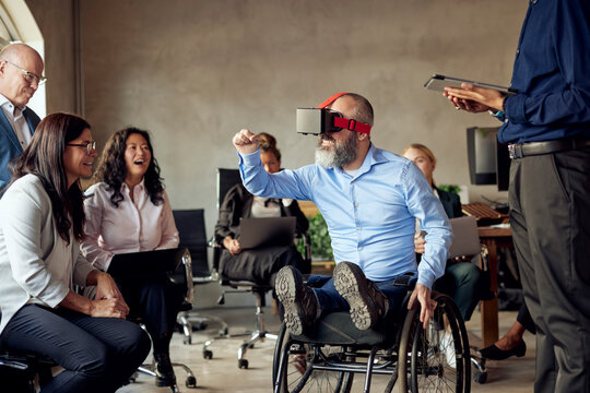 Male and female colleagues looking at businessman with disability watching VR at creative office