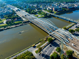 New triple tied-arc railroad bridge with four tracks, footbridge and bicycle lane over Vistula river in Krakow, Poland. Far view of new Krakow Zablocie railway station. Aerial view