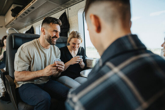 Happy parents playing cards with children while traveling in train