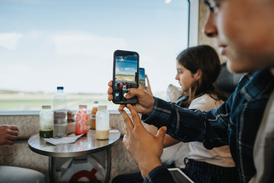 Boy capturing scenics through smart phone while traveling in train