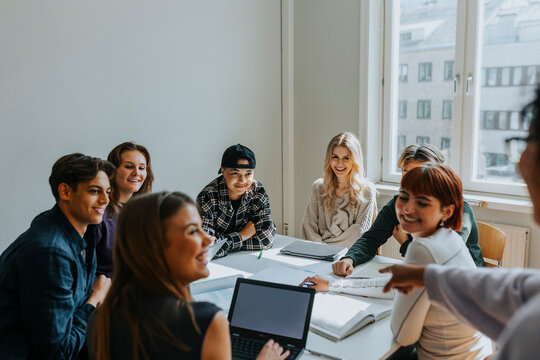 Smiling students looking at teacher pointing in classroom