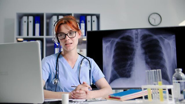 female doctor with headset talks to a patient via video link on a laptop and shows an x-ray image during an online medical consultation while sitting in medical office