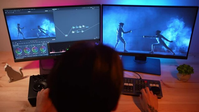 Over head shot of man working at the desk on speed mixer editor looking at monitor editing fencing video settings.