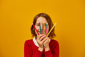 Portrait teen school girl covering her face with colored pencils