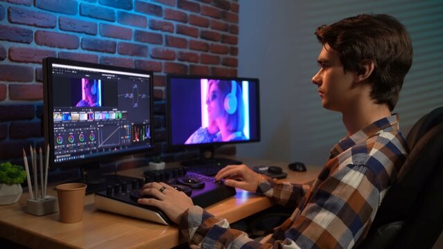 Portrait of young man in casual at the desk working on pc, looking in monitors, editing video with special equipment.
