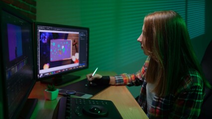 Side view of young female sitting at the desk looking in monitors editing video, correcting...