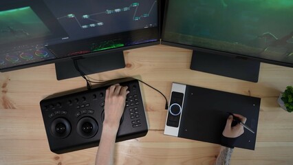 Top view of monitors and male hands working on computer at the desk at home, editing video using...
