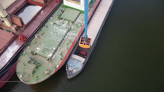 Aerial drone footage of a bulk carrier cargo ship being unloaded by a crane at a port. Bulk cargo tanker loading at a port seen from a bird's eye view.