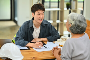 Asian architect man pointing on blueprint and explaining project plan to senior female clients at office