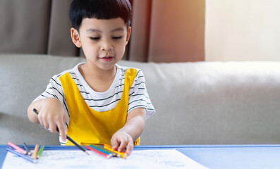 Portrait picture of little kids Asian boy smilling while drawing and coloring in his art book at desk in the living room.