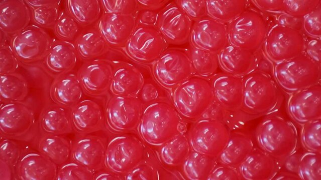 Pomegranate bobas for bubble tea made with agar agar and fruit juice in a container. Slow motion overhead view.