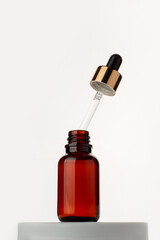 Drop falls from a pipette into a cosmetic bottle, isolated on white background.