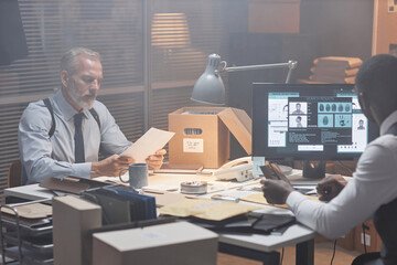 Moody portrait of two police detectives studying case in retro styled office, copy space