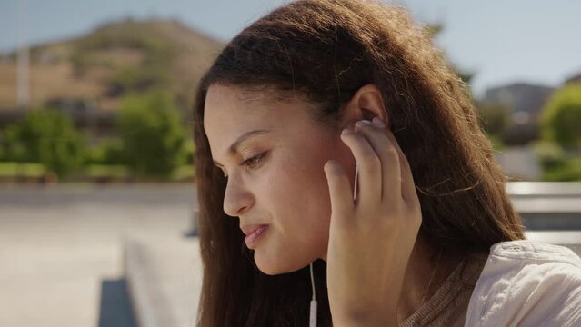Happy young multiracial woman in casual clothing putting in headphones at the skatepark